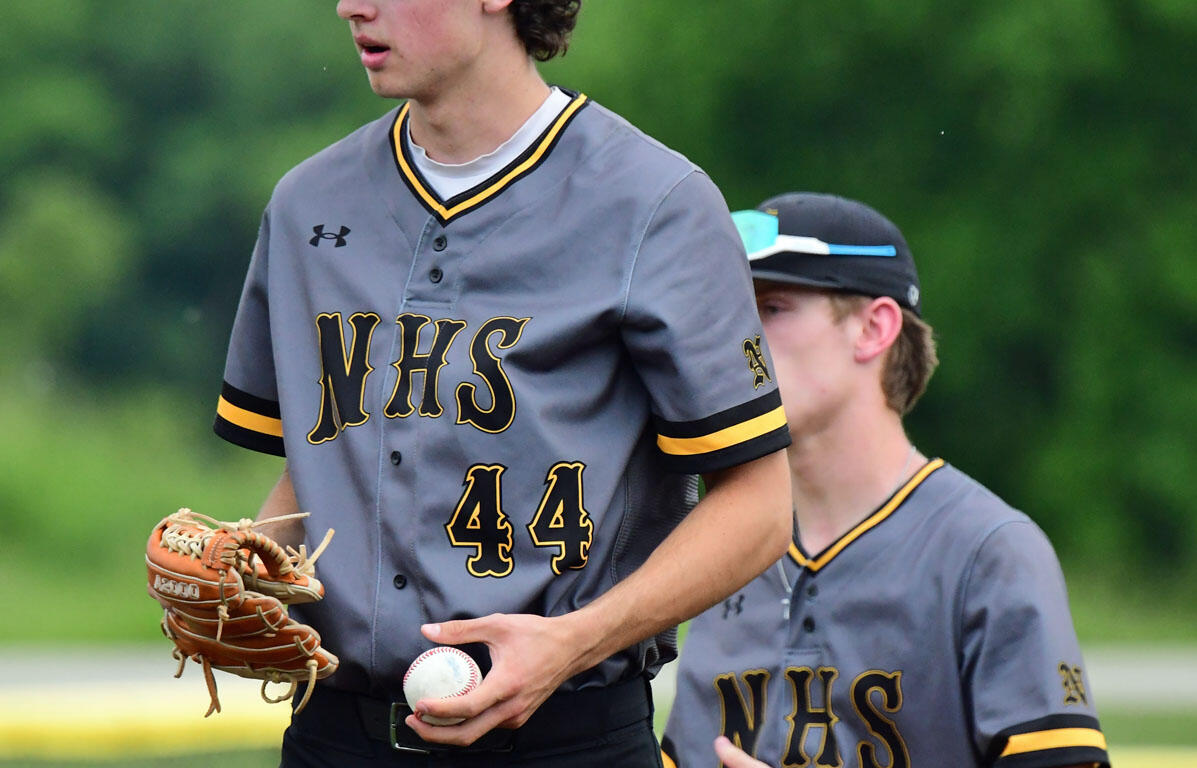 Two young baseball players in gray NHS uniforms on a field; foreground player holds a glove and baseball, ready to throw or field.**