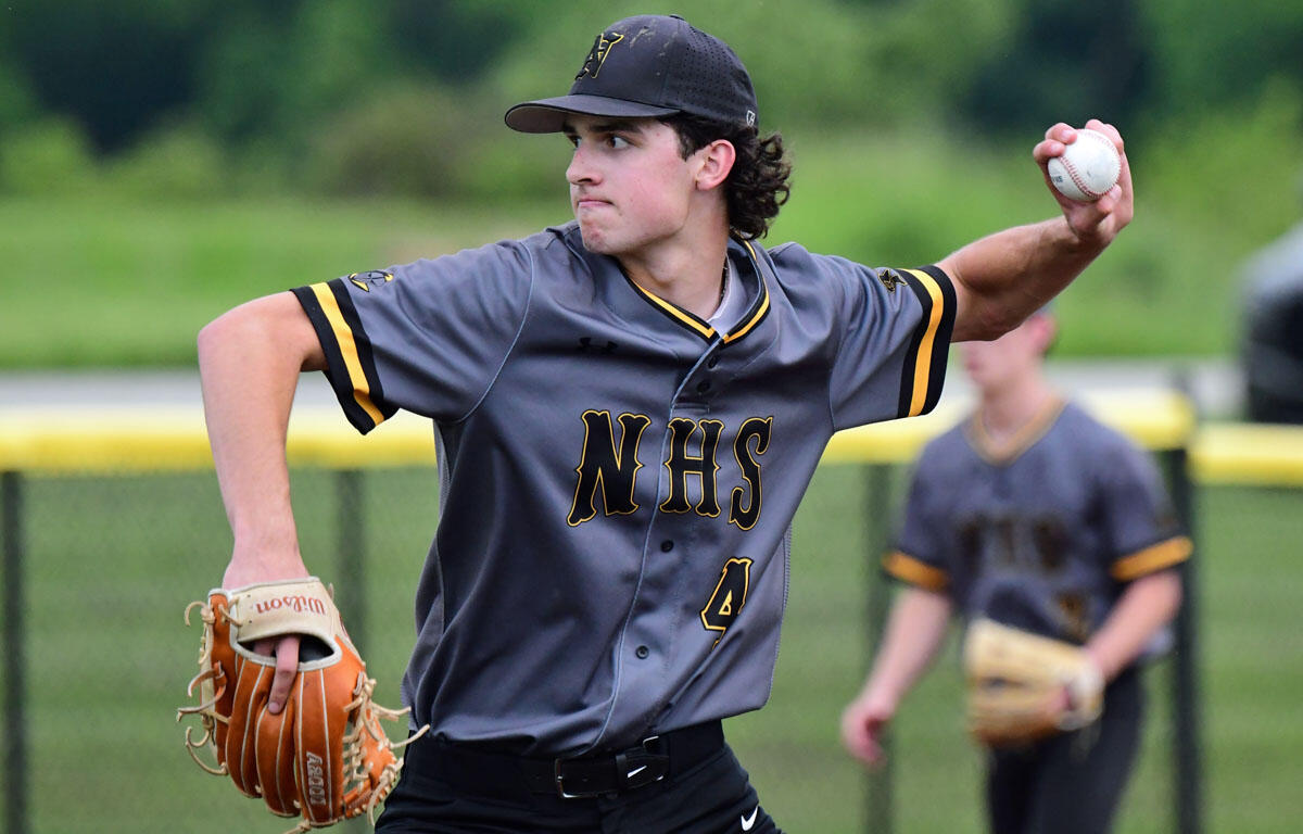Young baseball pitcher in gray NHS jersey throws a pitch with their right arm extended and a glove on the left hand on a baseball field.