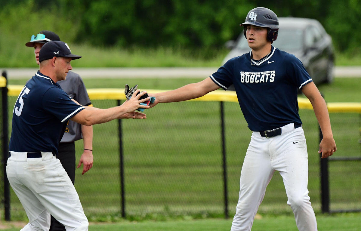 Two baseball players in navy jerseys high-five on a grassy field during a game on a sunny day.