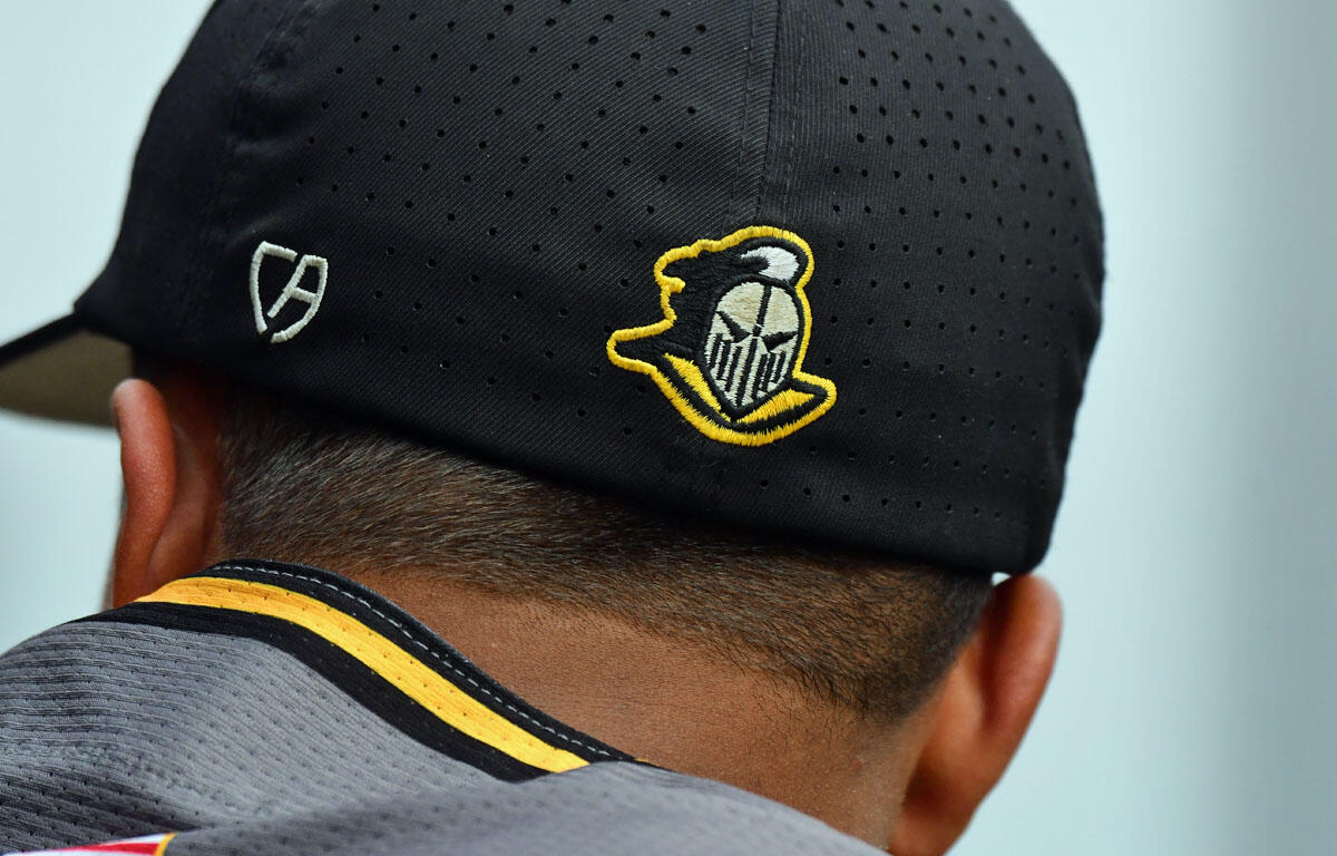 Back of a person’s head wearing a black perforated baseball cap with a yellow-outlined knight helmet logo on the side and a gray jersey visible below the cap.