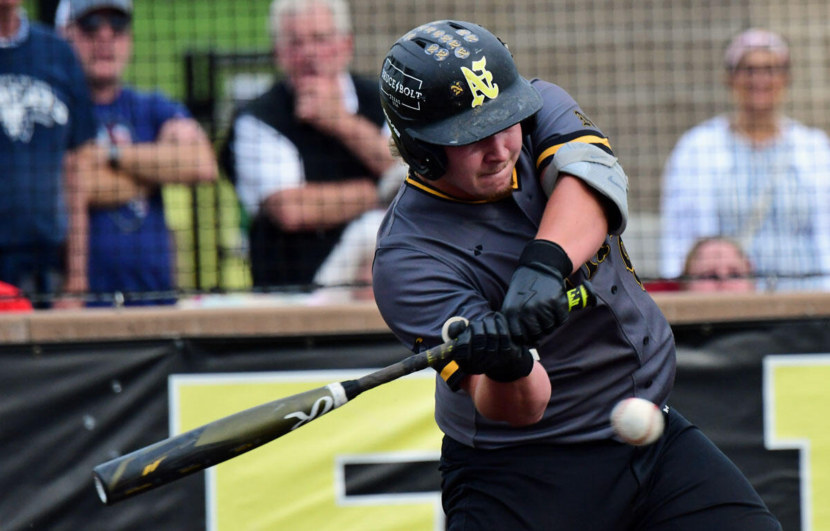 Baseball player in gray and black swings a bat at a pitched ball during a game with spectators in the background.