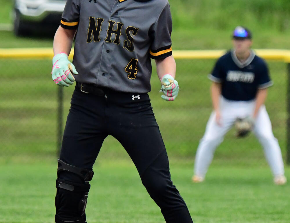 Baseball player wearing a gray NHS jersey with number 4, helmet, and teal gloves stands ready on the infield.