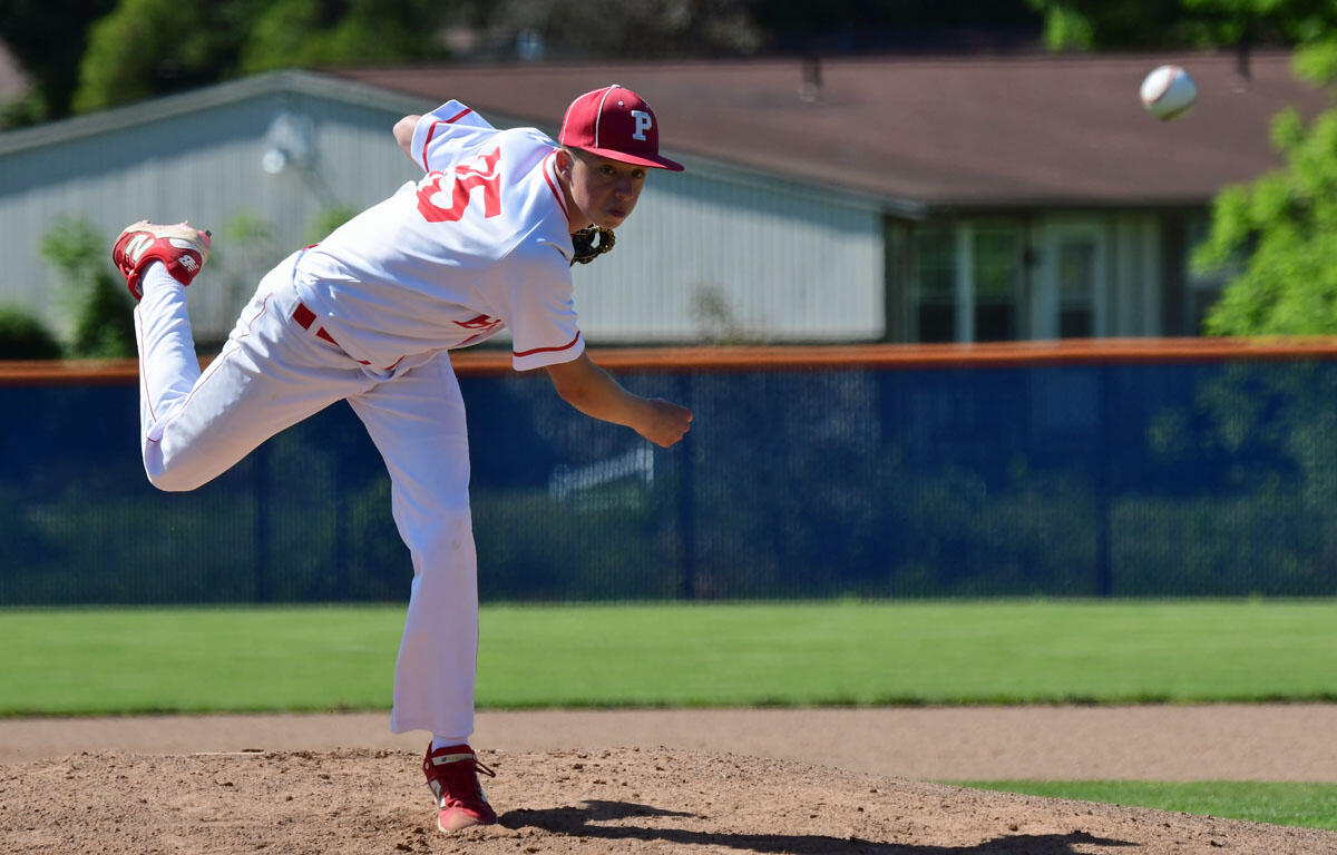 Baseball pitcher in white uniform with red cap (#5) mid‑throw on the mound, ball in the air behind him.