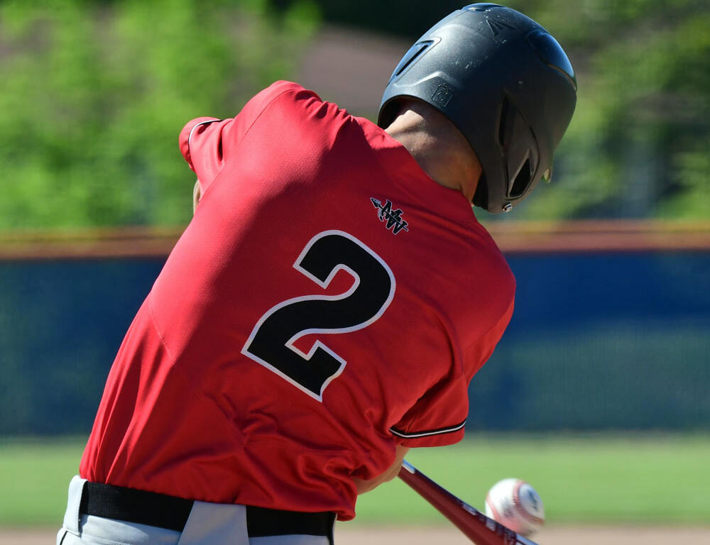 Baseball batter in a red jersey with number 2 swings a bat at a pitched ball during a game.
