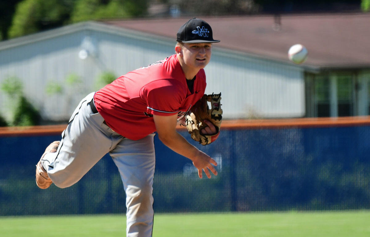 Young baseball pitcher in a red jersey winds up to throw, glove on his left hand as the ball sails by.