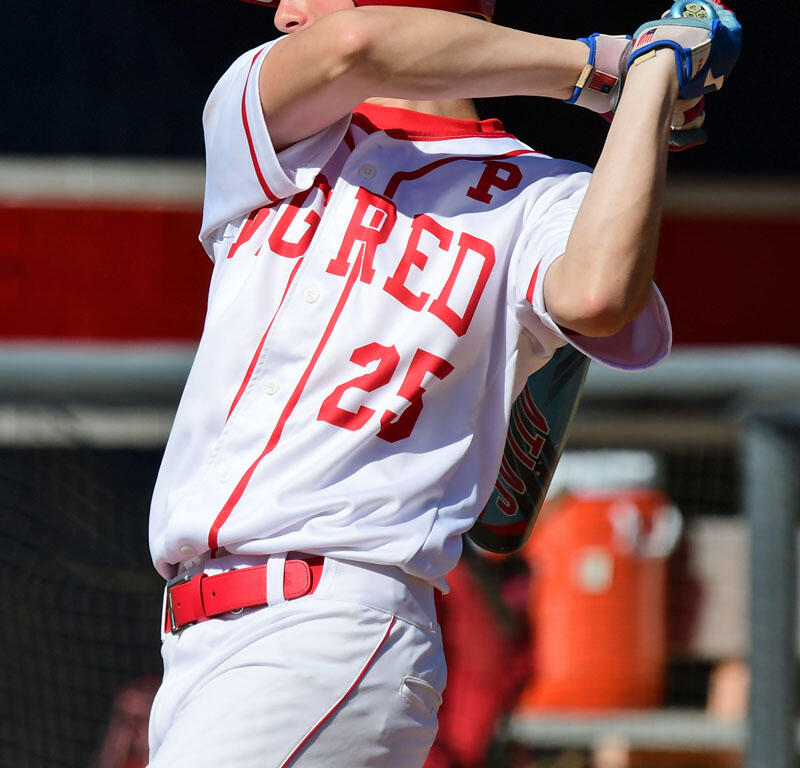 Baseball batter in a red helmet and white uniform swinging a bat during a game, number 25 visible on the jersey 2010s style.