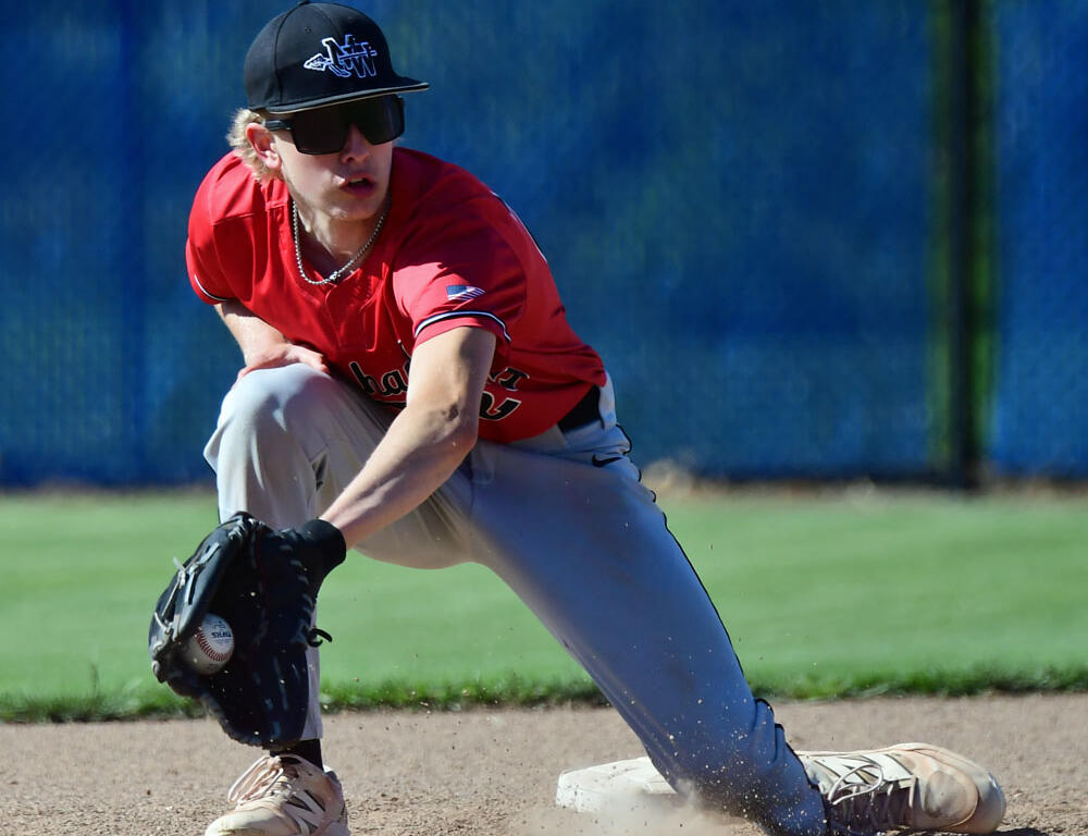 Baseball player in a red uniform slides into a base, glove reaching to field a ground ball