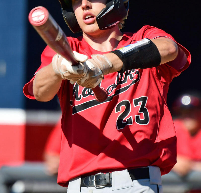 Baseball batter in a red uniform swings a bat during a game, wearing a helmet labeled MV