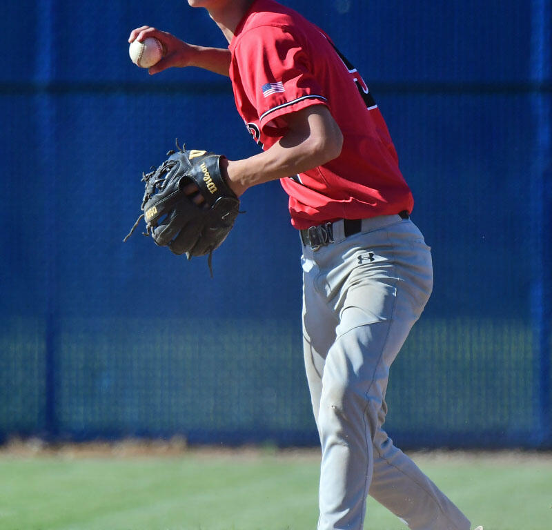 Young baseball pitcher in red jersey and cap throwing a pitch on the mound, glove ready at his side