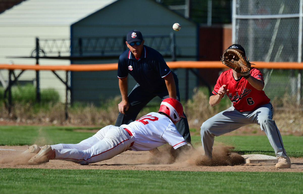 Baseball action: runner slides into a base as a fielder reaches with a glove and the ball is in midair nearby.