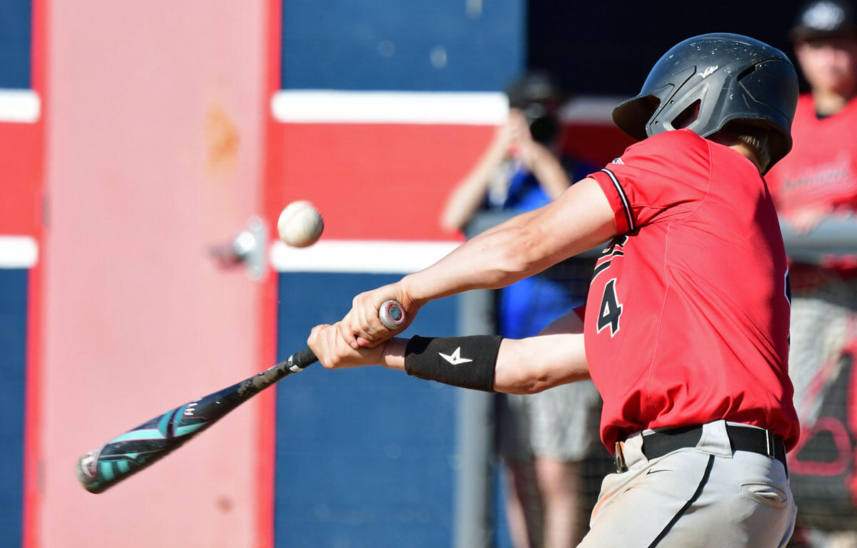 Baseball batter in a red jersey and helmet swings a bat at a pitched ball near the plate; ball midair approaching the bat.