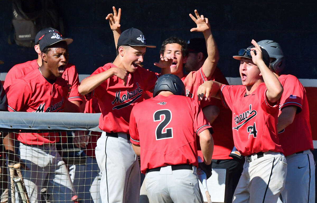 Baseball teammates in red uniforms celebrate at the dugout, raising arms and high-fiving each other.