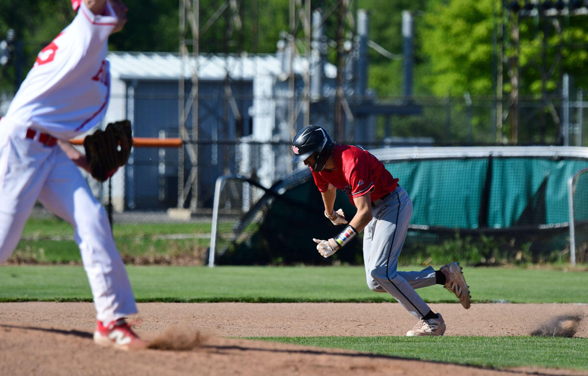 Baserunner in red slides toward a base as the pitcher throws from the mound in the foreground.