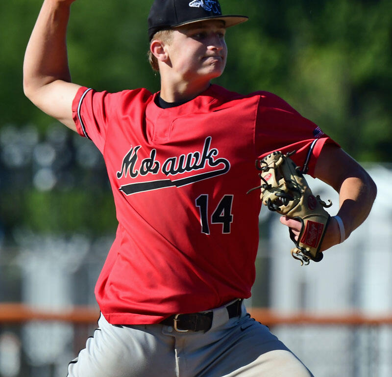 Young baseball pitcher in red jersey throwing a pitch with right arm raised and glove on left hand, on a sunny field