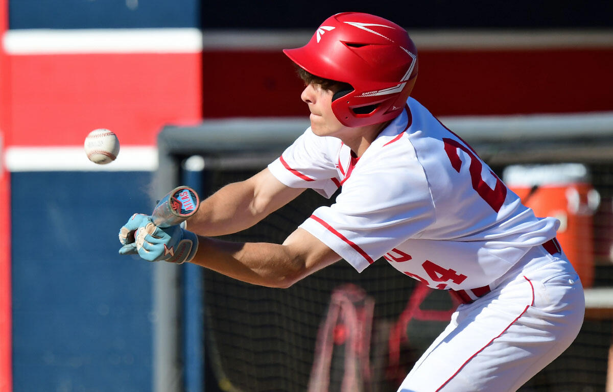 Baseball batter in a white-and-red uniform with a red helmet swinging at a pitched ball.
