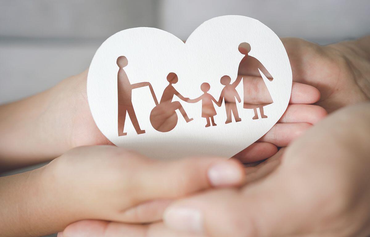 Paper heart cutout showing a family (parents, two children) holding hands, cradled in cupped hands to symbolize family support and care.