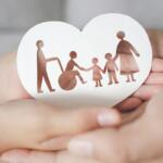 Paper heart cutout showing a family (parents, two children) holding hands, cradled in cupped hands to symbolize family support and care.