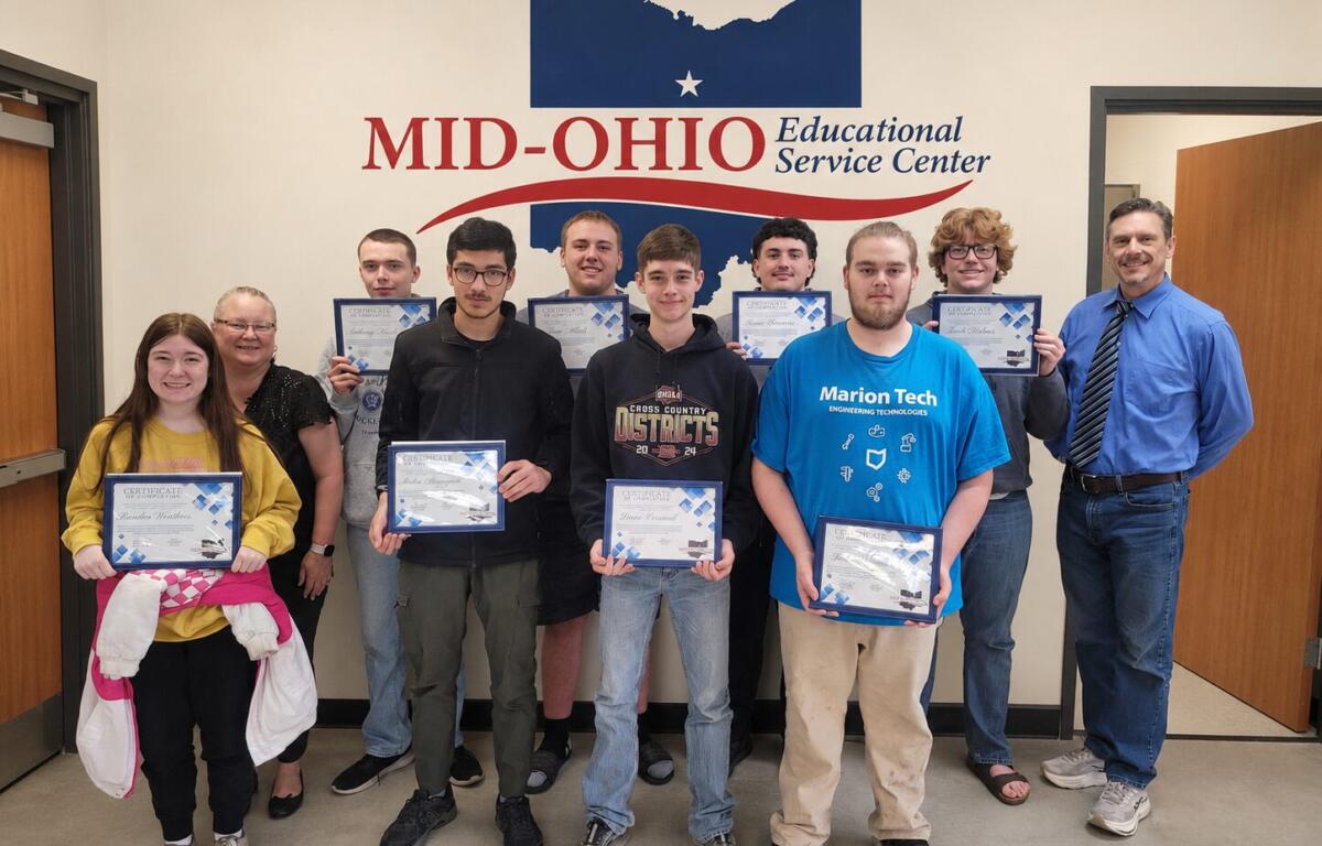Group of students and two adults posing with certificates in a hallway at Mid-Ohio Educational Service Center.