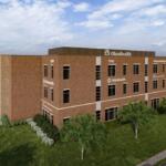 Three-story brick OhioHealth medical office building with parking lot and landscaped lawn, viewed from the grass.