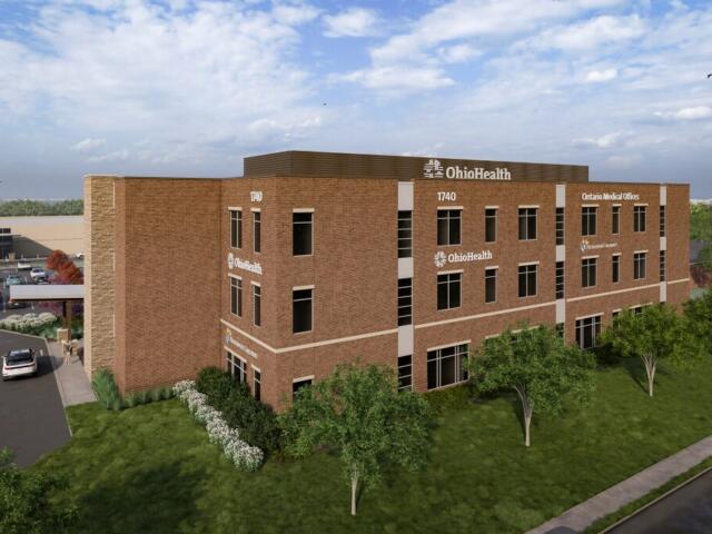 Three-story brick OhioHealth medical office building with parking lot and landscaped lawn, viewed from the grass.