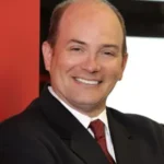 Smiling man in a dark suit and red tie, posing for a professional headshot.
