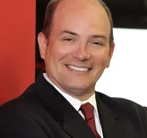 Smiling man in a dark suit and red tie, posing for a professional headshot.