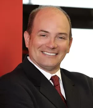Smiling man in a dark suit and red tie, posing for a professional headshot.