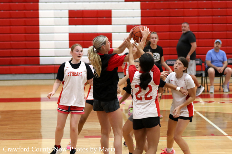 Youth girls' basketball game indoors; players jump for a loose ball near the basket in a crowded scramble for possession.