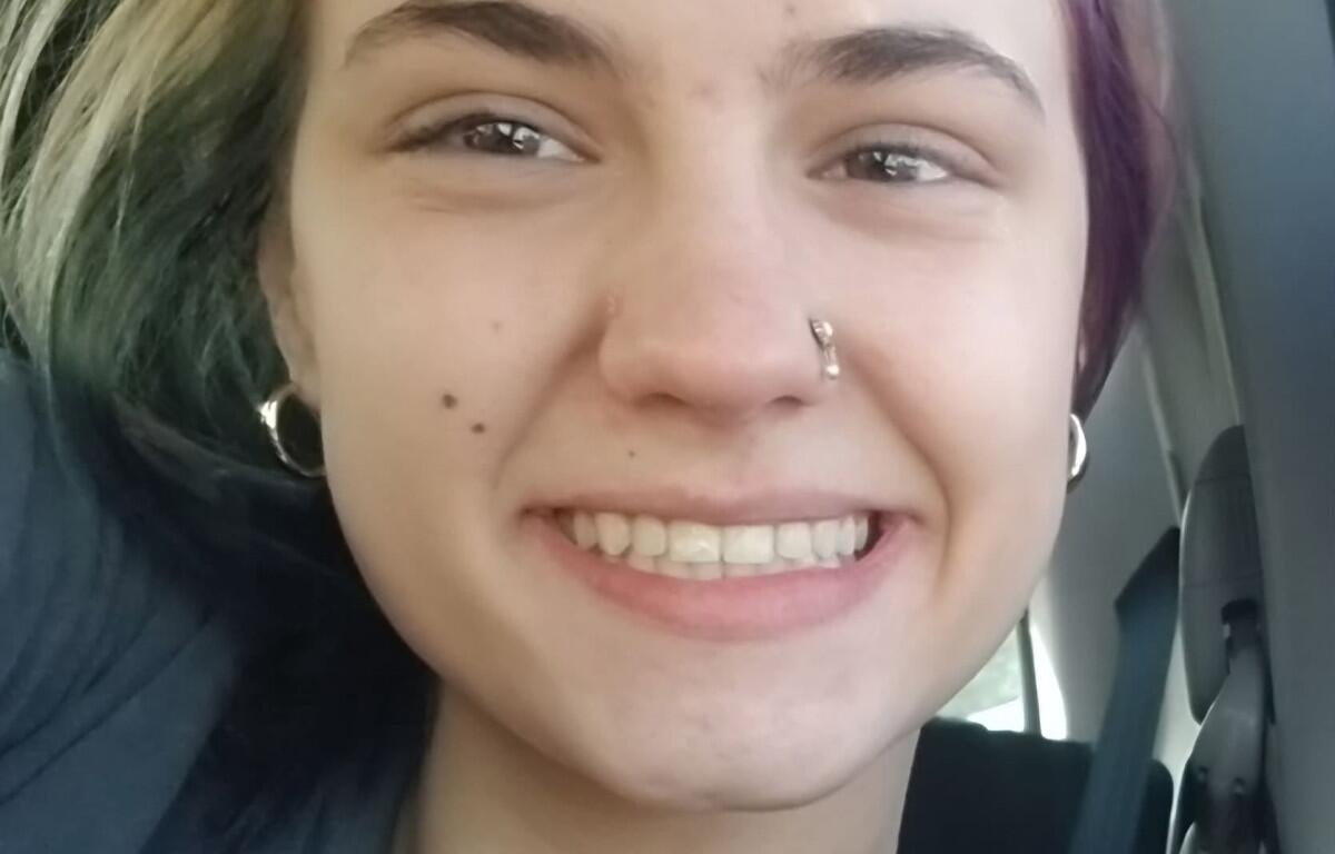 Close-up of a person smiling in a car, with a nose hoop and silver hoop earrings visible.