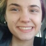 Close-up of a person smiling in a car, with a nose hoop and silver hoop earrings visible.