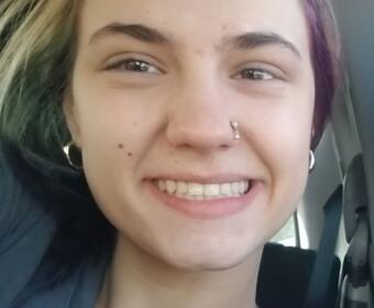 Close-up of a person smiling in a car, with a nose hoop and silver hoop earrings visible.