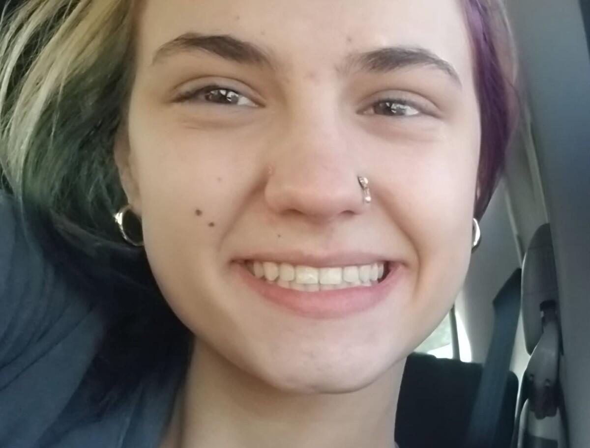 Close-up of a person smiling in a car, with a nose hoop and silver hoop earrings visible.