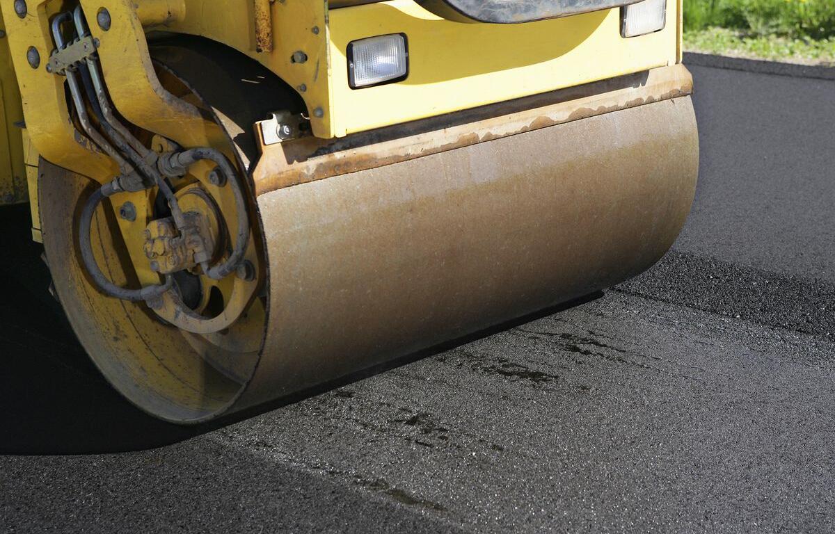 Yellow road roller compacting fresh asphalt on a road surface