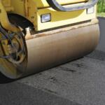 Yellow road roller compacting fresh asphalt on a road surface