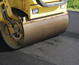 Yellow road roller compacting fresh asphalt on a road surface