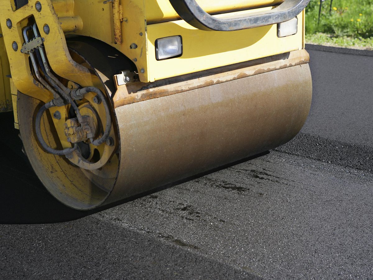 Yellow road roller compacting fresh asphalt on a road surface