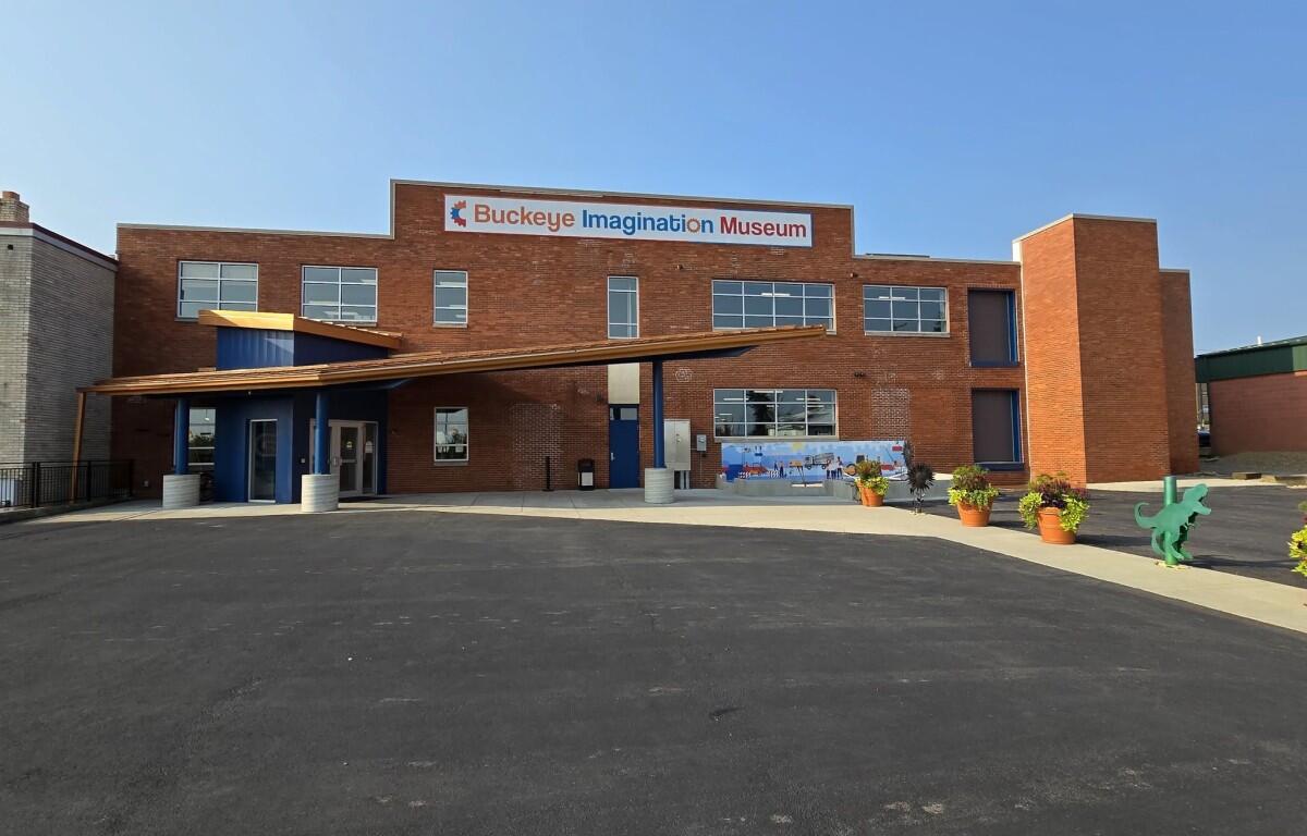 Brick exterior of Buckeye Imagination Museum with a blue entry canopy and potted plants outside the entrance.