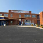 Brick exterior of Buckeye Imagination Museum with a blue entry canopy and potted plants outside the entrance.