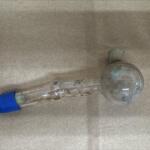 Dirty glass laboratory tube with a round bulb at one end and blue stopper on the other, lying on a bare concrete surface (informational).