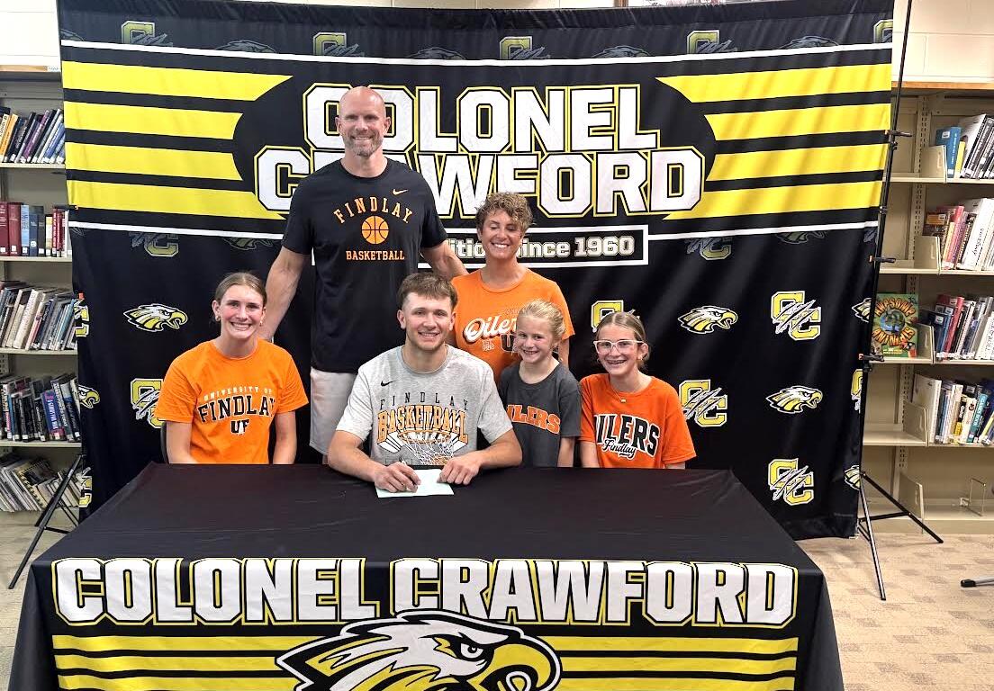Group of students and a coach posing at a signing event in front of a Colonel Crawford banner and table cover featuring the eagle mascot.