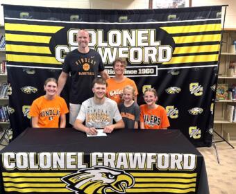 Group of students and a coach posing at a signing event in front of a Colonel Crawford banner and table cover featuring the eagle mascot.