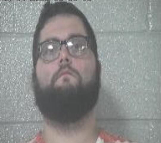Man with a dark beard and glasses facing the camera against a gray cinder block wall; timestamp overlay in the top-left corner.