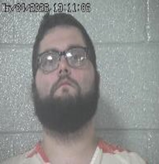 Man with a dark beard and glasses facing the camera against a gray cinder block wall; timestamp overlay in the top-left corner.