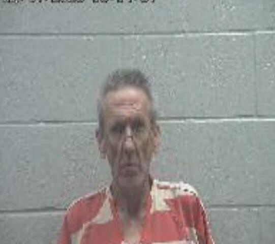 Mugshot of a middle-aged man in an orange-and-white striped jumpsuit standing against a gray cinder block wall, timestamp at top left.