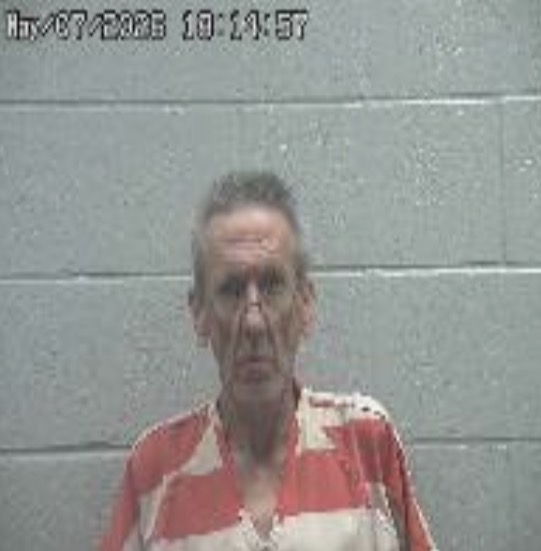 Mugshot of a middle-aged man in an orange-and-white striped jumpsuit standing against a gray cinder block wall, timestamp at top left.