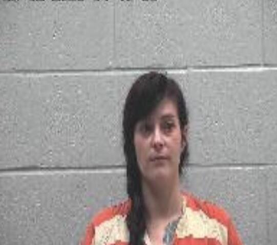 Mugshot of a woman in an orange jail uniform with a braid, against a gray cinder block wall; timestamp shown in top-left.