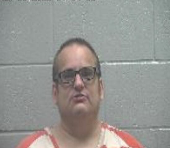 Mugshot of a man in an orange-striped jail uniform against a gray cinder-block wall; timestamp visible in the top-left.