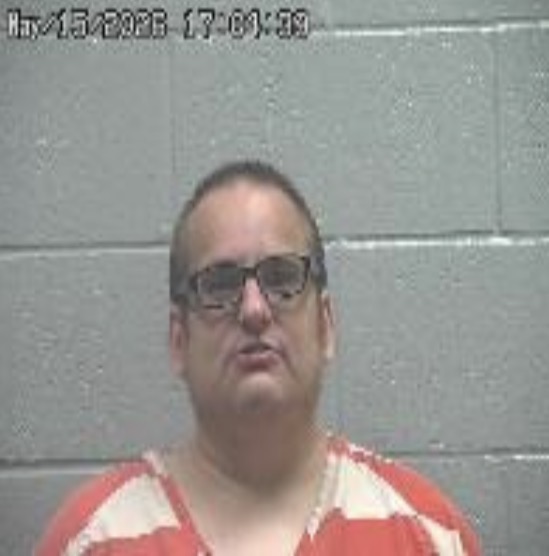 Mugshot of a man in an orange-striped jail uniform against a gray cinder-block wall; timestamp visible in the top-left.
