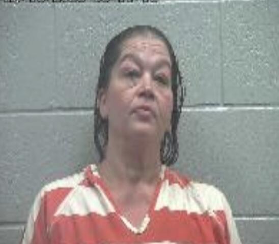 Mugshot of a woman in red-and-white striped jail uniform against a gray cinder block wall; timestamp visible in the top-left corner.