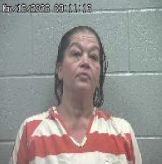 Mugshot of a woman in red-and-white striped jail uniform against a gray cinder block wall; timestamp visible in the top-left corner.